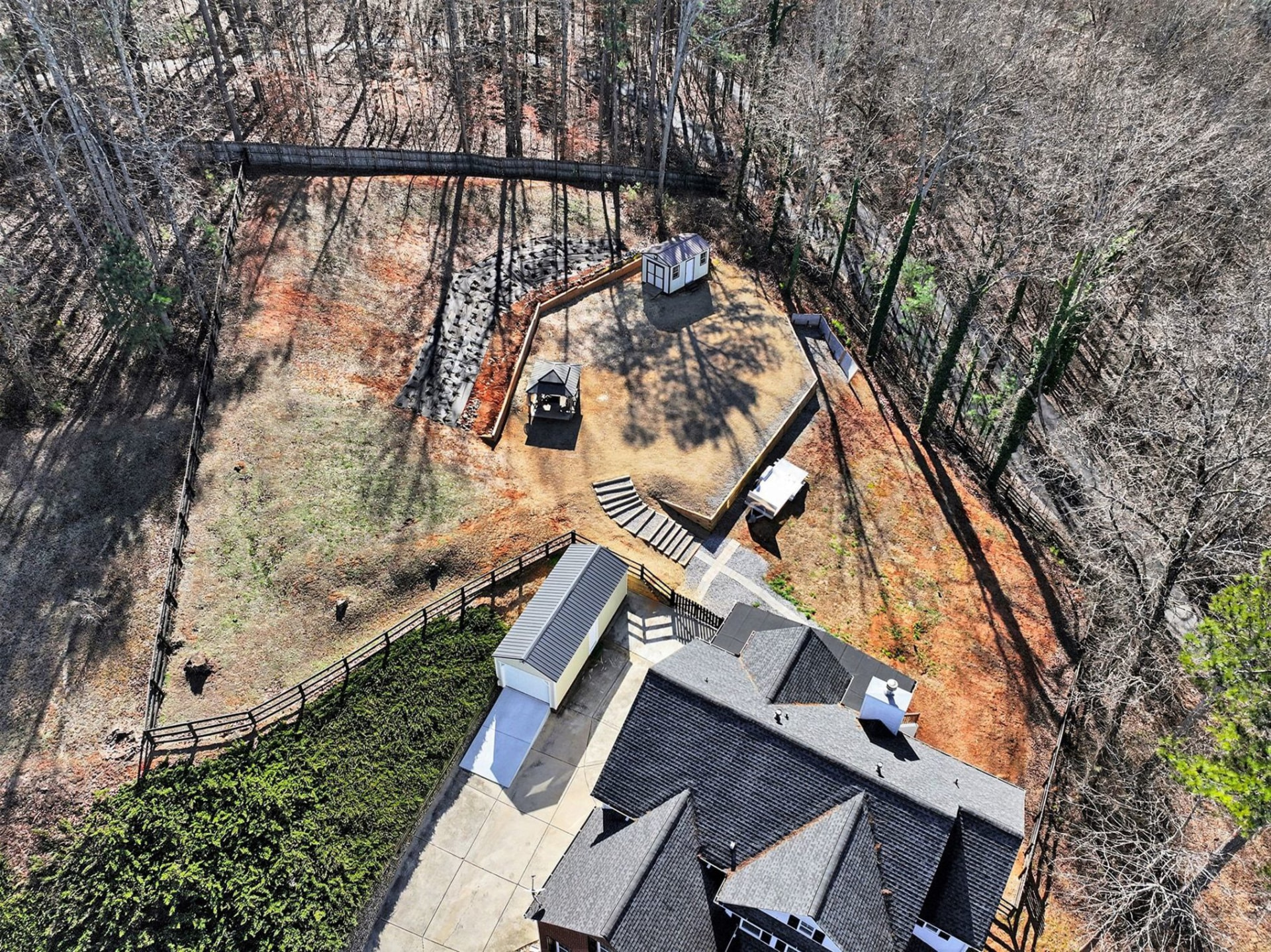 Aerial view of the fenced rear yard with a storage building, gazebo and wooded tree line