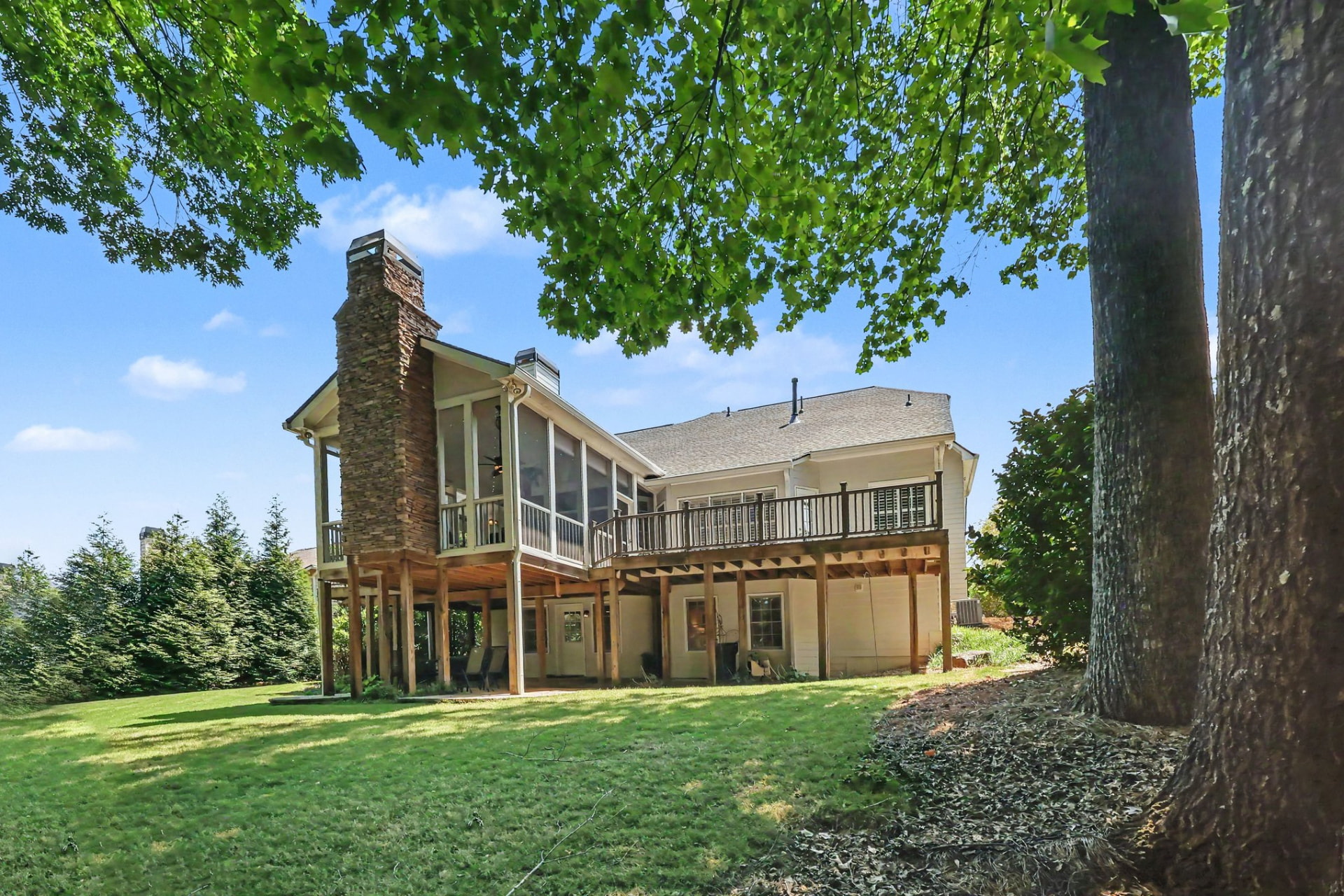 Rear elevation with a stone chimney and screened porch above a sloping lawn