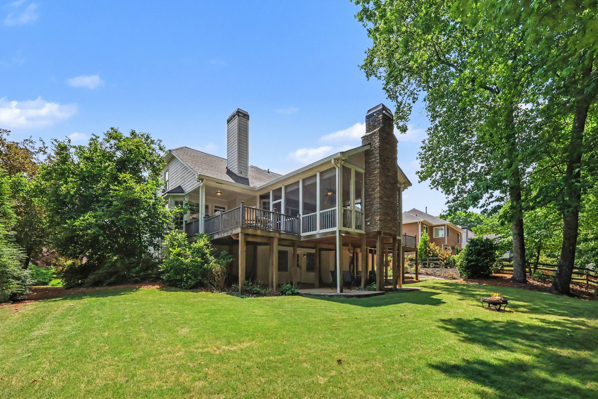 Level back lawn with a fire pit below the home's deck and screened porch